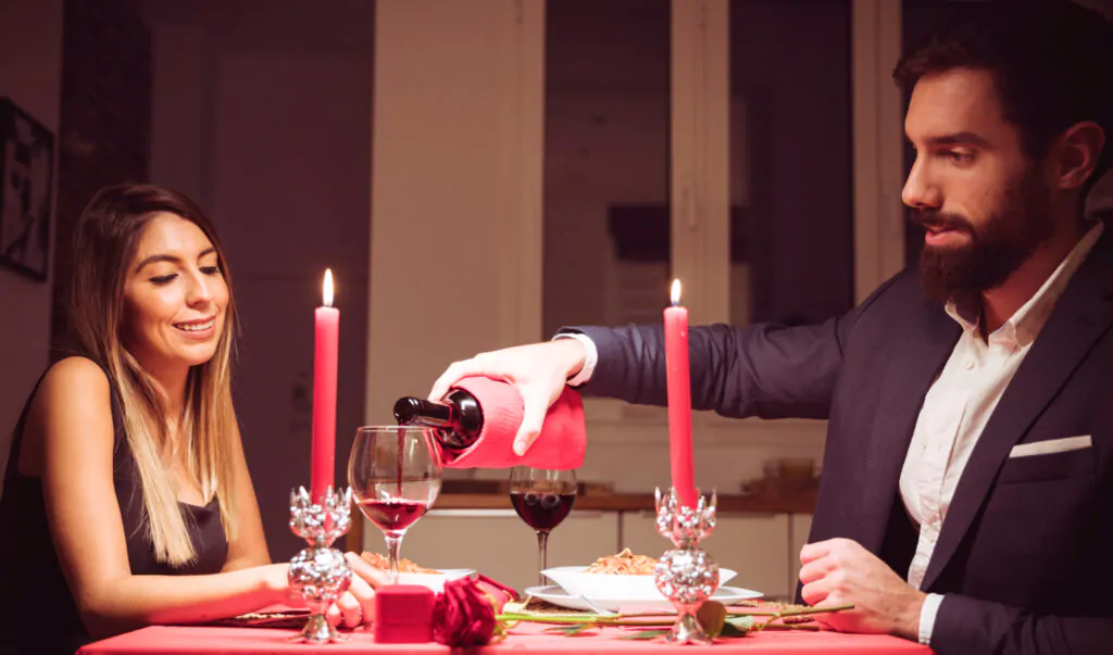 dicas sobre o que fazer para o dia dos namorados: jantar romântico de casal, com o home servindo vinho para a mulher.