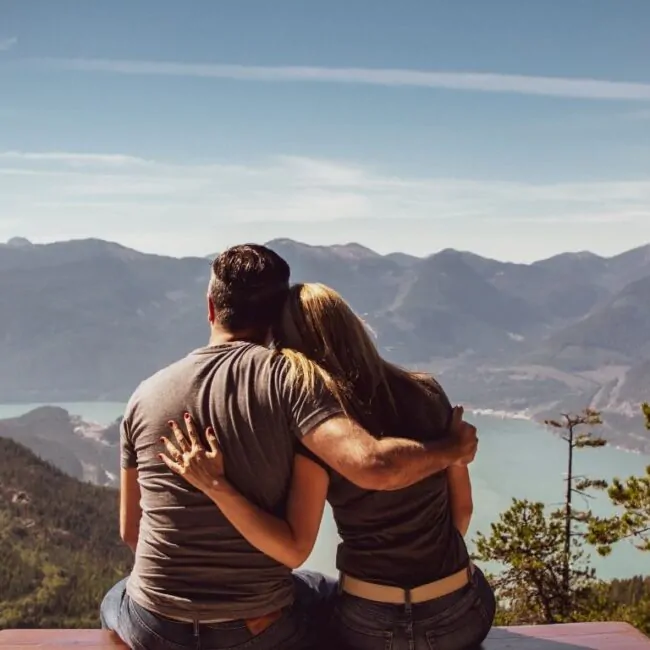 Casal sentados em uma montanha abraçados olhando a vista.